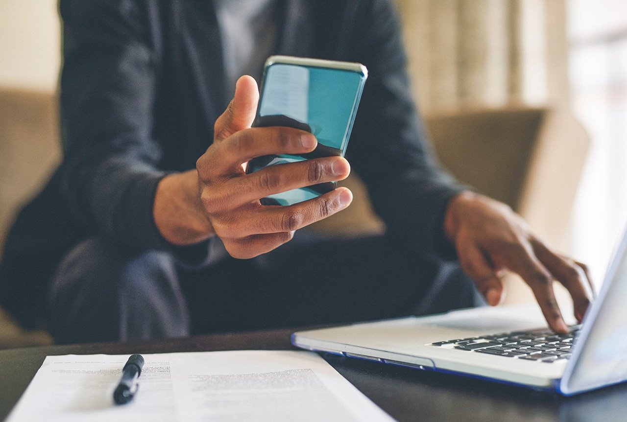 Un homme qui utilise un téléphone cellulaire et un ordinateur, tous deux des produits électroniques grand public